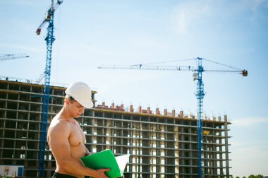 Çıplak bir gövde ile genç seksi erkek vücut geliştirmeci atlet. İnşaat yapı ve inşaat vinç belgeler ile arka plan üzerinde beyaz koruyucu kask Yöneticisi mühendis Oluşturucu standları