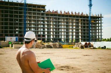 Çıplak bir gövde ile genç seksi erkek vücut geliştirmeci atlet. İnşaat yapı ve inşaat vinç belgeler ile arka plan üzerinde beyaz koruyucu kask Yöneticisi mühendis Oluşturucu standları