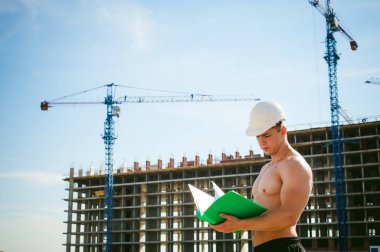 Çıplak bir gövde ile genç seksi erkek vücut geliştirmeci atlet. İnşaat yapı ve inşaat vinç belgeler ile arka plan üzerinde beyaz koruyucu kask Yöneticisi mühendis Oluşturucu standları