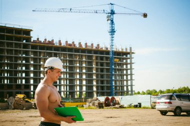 Çıplak bir gövde ile genç seksi erkek vücut geliştirmeci atlet. İnşaat yapı ve inşaat vinç belgeler ile arka plan üzerinde beyaz koruyucu kask Yöneticisi mühendis Oluşturucu standları