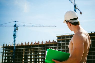 Çıplak bir gövde ile genç seksi erkek vücut geliştirmeci atlet. İnşaat yapı ve inşaat vinç belgeler ile arka plan üzerinde beyaz koruyucu kask Yöneticisi mühendis Oluşturucu standları