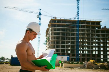 Çıplak bir gövde ile genç seksi erkek vücut geliştirmeci atlet. İnşaat yapı ve inşaat vinç belgeler ile arka plan üzerinde beyaz koruyucu kask Yöneticisi mühendis Oluşturucu standları