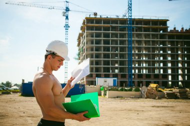 Çıplak bir gövde ile genç seksi erkek vücut geliştirmeci atlet. İnşaat yapı ve inşaat vinç belgeler ile arka plan üzerinde beyaz koruyucu kask Yöneticisi mühendis Oluşturucu standları