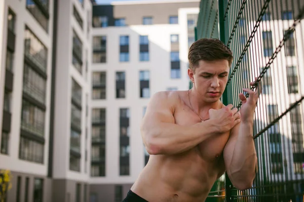 Yakışıklı seksi erkek vücut geliştirmeci sporcu adam çıplak gövde ile bir güçlü kas vücut ayakta gösterilen pozlar courtyard bir yeşil kılavuz çit spor alanında yakınındaki. Sağlıklı yaşam konsepti.