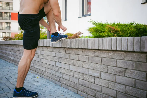 Bonito homem atleta fisiculturista sexy masculino com tronco nu, correndo de manhã, ao ar livre. amarra atacadores em ténis. Conceito de estilo de vida saudável . — Fotografia de Stock