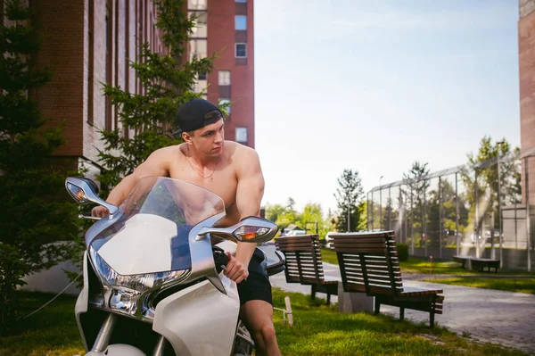 Hombre atractivo atleta sexy con torso desnudo en el patio de la casa en el estacionamiento sentado en una motocicleta deportiva blanca, una mañana de verano temprano soleado — Foto de Stock