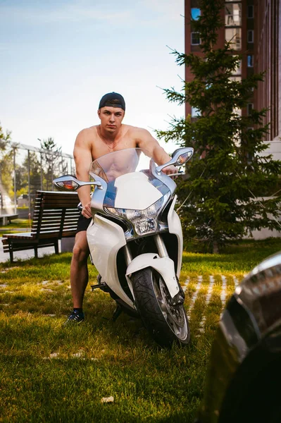 Hombre atractivo atleta sexy con torso desnudo en el patio de la casa en el estacionamiento sentado en una motocicleta deportiva blanca, una mañana de verano temprano soleado —  Fotos de Stock