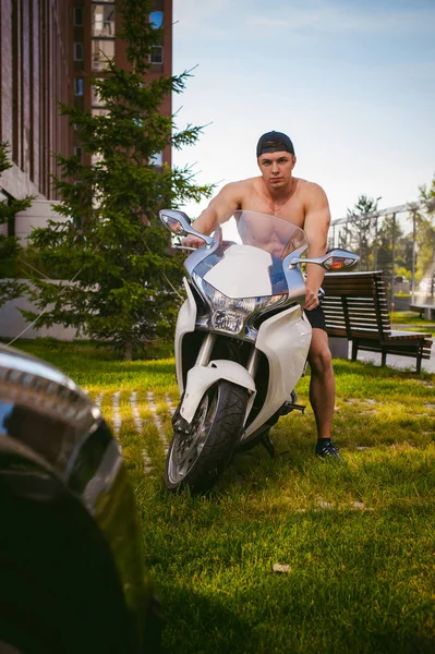 Schöner sexy männlicher Athlet Mann mit nacktem Oberkörper im Hof des Hauses auf dem Parkplatz sitzend auf einem weißen Sportmotorrad, ein früher sonniger Sommermorgen — Stockfoto