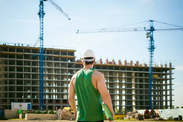 Genç seksi erkek vücut geliştirmeci atlet. Müdür mühendis Oluşturucu koruyucu kask yapı ve inşaat İnşaat arka plan üzerinde duran beyaz belgeleri ile el vinç