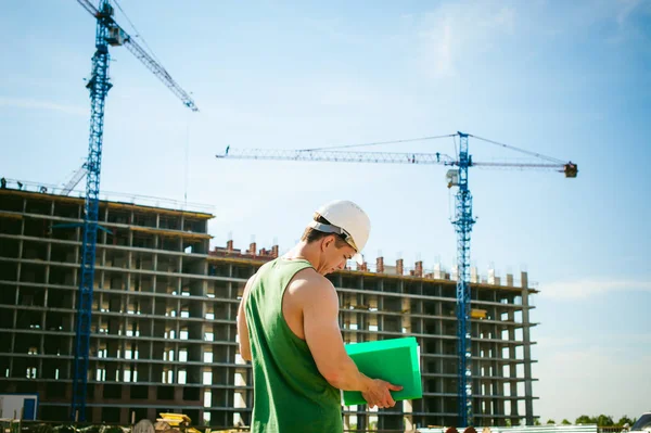 Genç seksi erkek vücut geliştirmeci atlet. Müdür mühendis Oluşturucu koruyucu kask yapı ve inşaat İnşaat arka plan üzerinde duran beyaz belgeleri ile el vinç