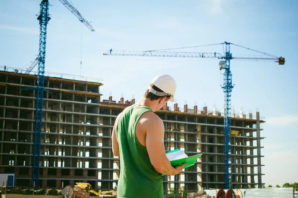 Genç seksi erkek vücut geliştirmeci atlet. Müdür mühendis Oluşturucu koruyucu kask yapı ve inşaat İnşaat arka plan üzerinde duran beyaz belgeleri ile el vinç