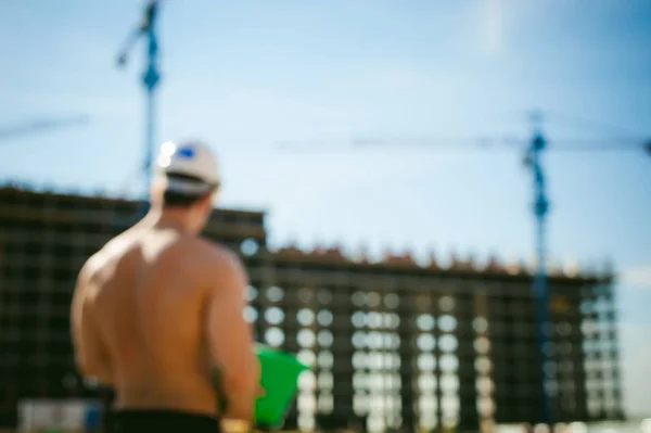 Молодий сексуальний спортсмен чоловічої статі з голим торсом. Менеджер інженер-будівельник в білому захисному шоломі стоїть на тлі будівництва будівельних і будівельних кранів з документацією — стокове фото