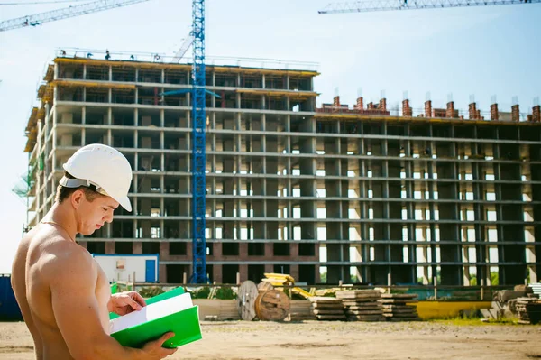Genç seksi erkek vücut geliştirmeci atlet. Müdür mühendis Oluşturucu koruyucu kask yapı ve inşaat İnşaat arka plan üzerinde duran beyaz belgeleri ile el vinç