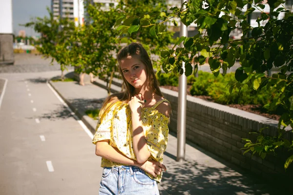 Jovem mulher bonita está passeando ao ar livre no quintal, contra o pano de fundo de vegetação e casas, verão quente dia ensolarado — Fotografia de Stock