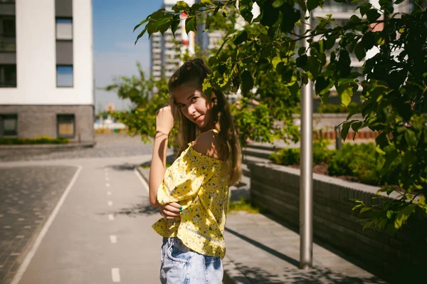 Jeune belle femme se promène à l'extérieur dans la cour, sur fond de verdure et de maisons, chaude journée ensoleillée d'été — Photo