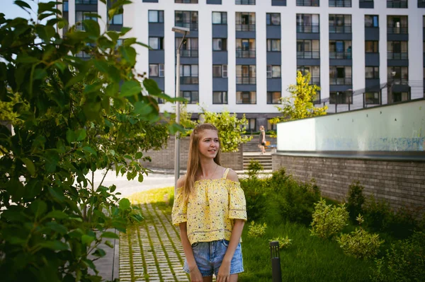 Jovem mulher bonita está passeando ao ar livre no quintal, contra o pano de fundo de vegetação e casas, verão quente dia ensolarado — Fotografia de Stock