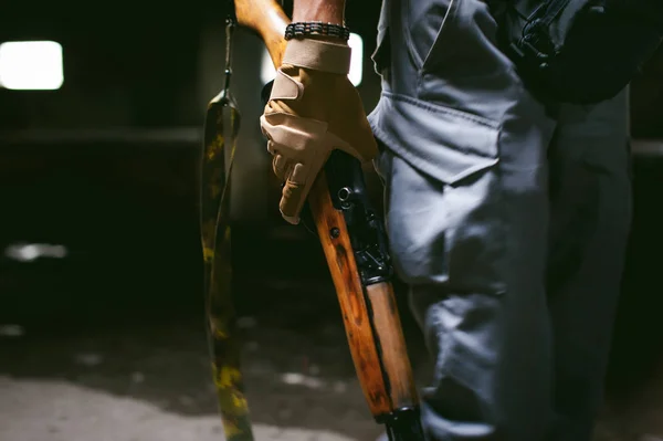 Lekkoatletycznego mężczyzna w szarym ubrania karabinek pistolet w ręku. Zbliżenie: rękawice taktyczne z broni — Zdjęcie stockowe