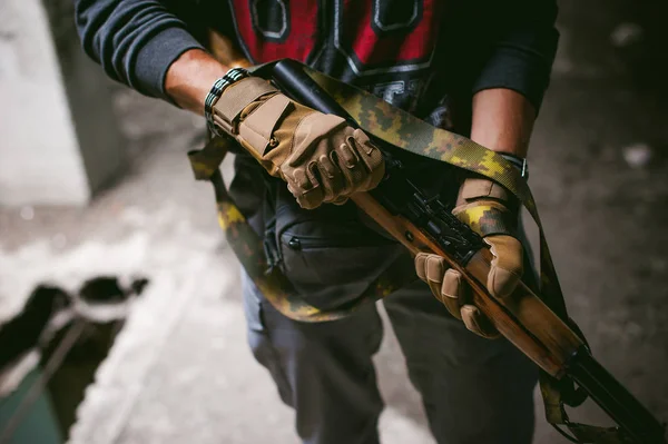 Lekkoatletycznego mężczyzna w szarym ubrania karabinek pistolet w ręku. Zbliżenie: rękawice taktyczne z broni — Zdjęcie stockowe