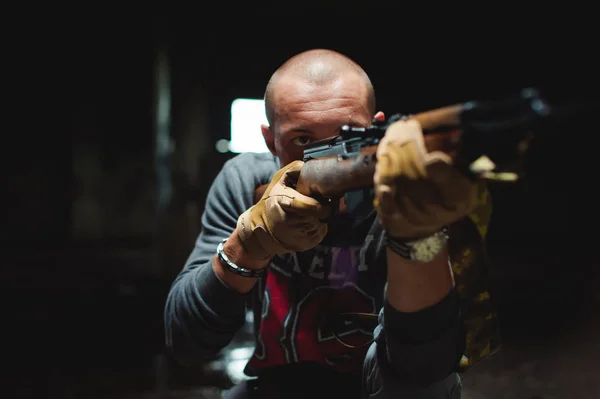 Lekkoatletycznego mężczyzna w szarym ubrania karabinek pistolet w ręku. Zbliżenie: rękawice taktyczne broni. Cel na odległość, widok z przodu — Zdjęcie stockowe