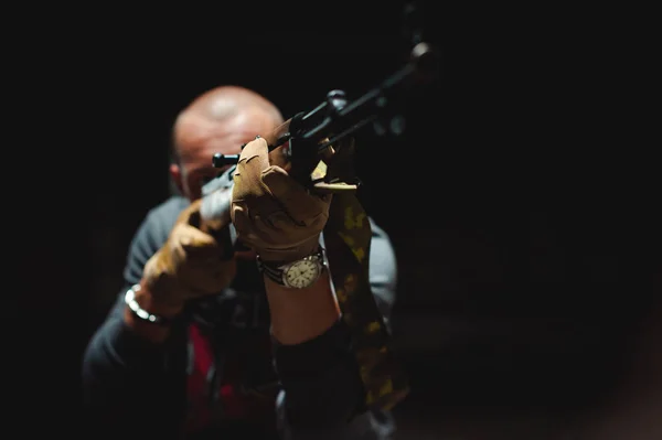 Lekkoatletycznego mężczyzna w szarym ubrania karabinek pistolet w ręku. Zbliżenie: rękawice taktyczne z broni, zegarek na rękę. Cel na odległość, widok z przodu. Wykonywanie misji bojowych — Zdjęcie stockowe