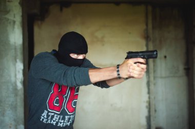 Atletik bir yün, kar maskesi kafasında, erkekte silah elinde tutuyor.