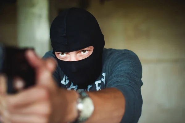 Athletic man in a balaclava, ski mask on his head, holds a gun in his hand