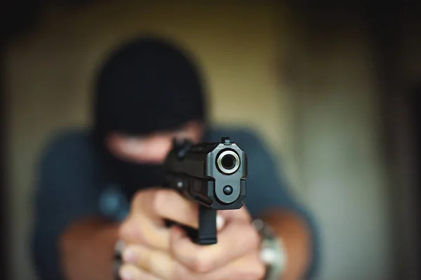 Hombre atlético en un pasamontañas, sostiene una pistola en su mano, es amenazado con disparar, apuntando —  Fotos de Stock