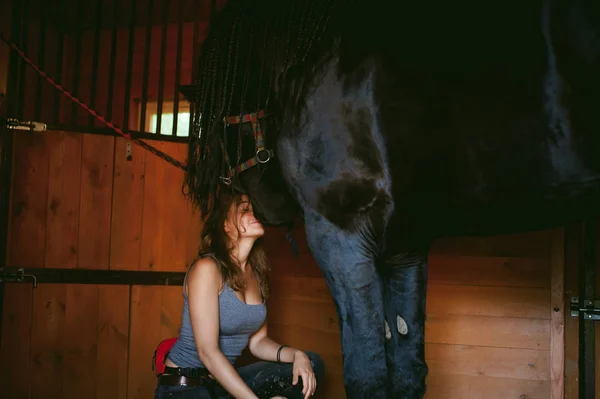女性騎手掃除ブラシ フリージアン馬の農場、馬小屋が付いている土から純血種のペットの世話 — ストック写真