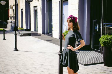 Karanlık bir şık elbiseli güzel kadın butikler yakınındaki cadde boyunca elini kolunu sallaya dönüyor. Bir moda kız portresi