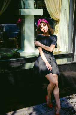 Karanlık bir şık elbiseli güzel kadın butikler yakınındaki cadde boyunca elini kolunu sallaya dönüyor. Bir moda kız portresi