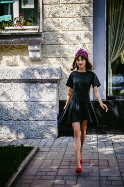 Karanlık bir şık elbiseli güzel kadın butikler yakınındaki cadde boyunca elini kolunu sallaya dönüyor. Bir moda kız portresi