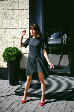 Karanlık bir şık elbiseli güzel kadın butikler yakınındaki cadde boyunca elini kolunu sallaya dönüyor. Bir moda kız portresi