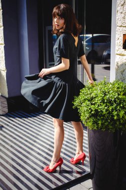 Karanlık bir şık elbiseli güzel kadın butikler yakınındaki cadde boyunca elini kolunu sallaya dönüyor. Bir moda kız portresi