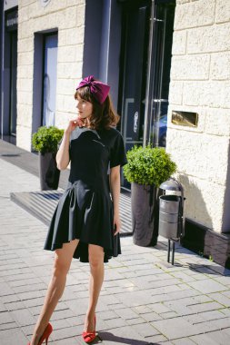 Karanlık bir şık elbiseli güzel kadın butikler yakınındaki cadde boyunca elini kolunu sallaya dönüyor. Bir moda kız portresi