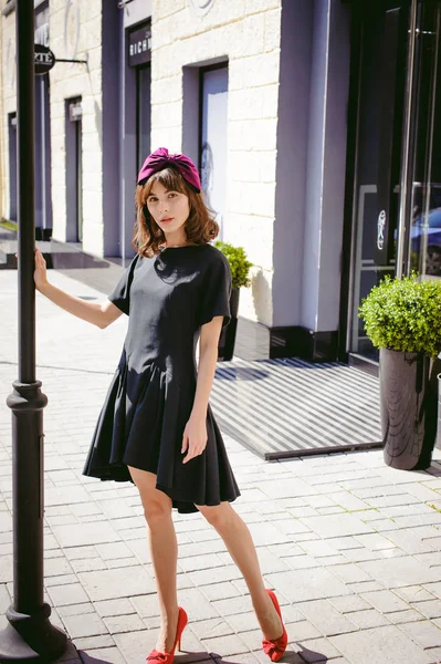 Beautiful woman in a dark stylish dress strolls along the street, near boutiques. Portrait of a fashionable girl — Stock Photo, Image