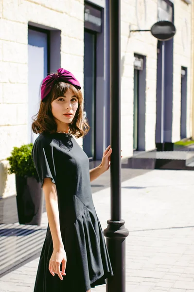 Karanlık bir şık elbiseli güzel kadın butikler yakınındaki cadde boyunca elini kolunu sallaya dönüyor. Bir moda kız portresi