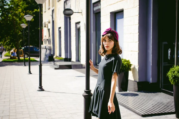 Beautiful woman in a dark stylish dress strolls along the street, near boutiques. Portrait of a fashionable girl — Stock Photo, Image