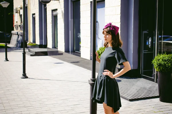 Karanlık bir şık elbiseli güzel kadın butikler yakınındaki cadde boyunca elini kolunu sallaya dönüyor. Bir moda kız portresi