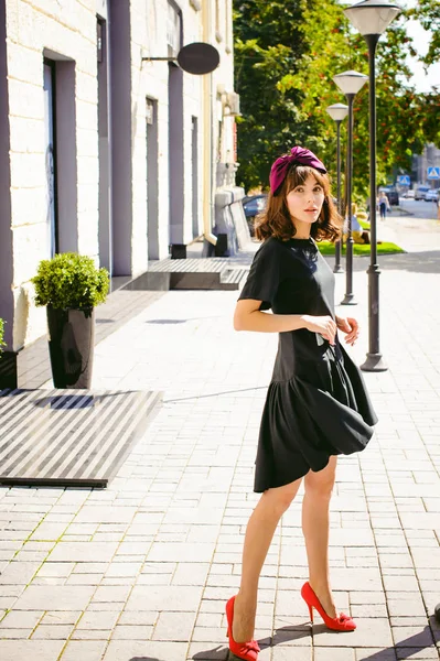 Karanlık bir şık elbiseli güzel kadın butikler yakınındaki cadde boyunca elini kolunu sallaya dönüyor. Bir moda kız portresi