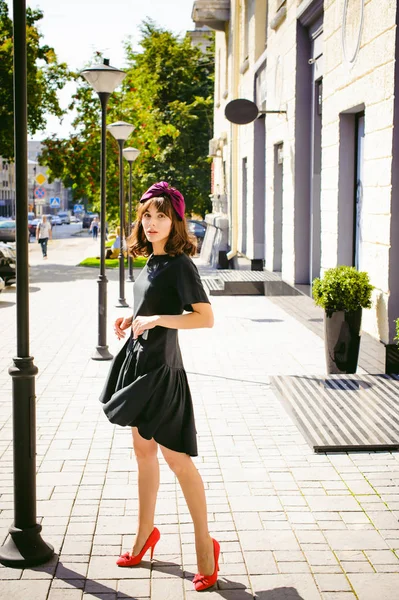 Beautiful woman in a dark stylish dress strolls along the street, near boutiques. Portrait of a fashionable girl — Stock Photo, Image