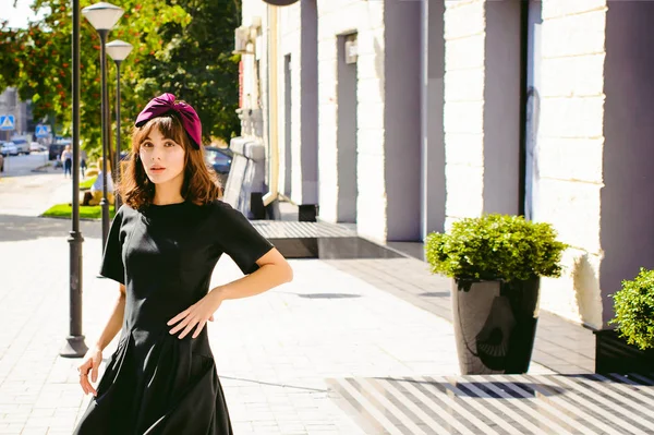 Karanlık bir şık elbiseli güzel kadın butikler yakınındaki cadde boyunca elini kolunu sallaya dönüyor. Bir moda kız portresi