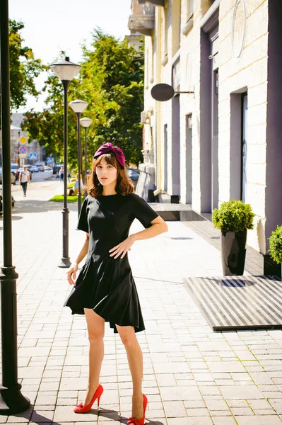 Beautiful woman in a dark stylish dress strolls along the street, near boutiques. Portrait of a fashionable girl — Stock Photo, Image