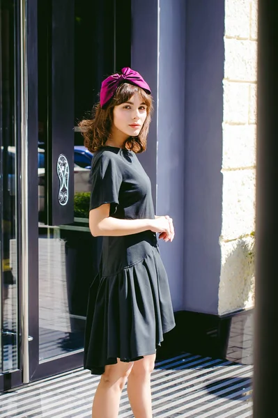 Karanlık bir şık elbiseli güzel kadın butikler yakınındaki cadde boyunca elini kolunu sallaya dönüyor. Bir moda kız portresi