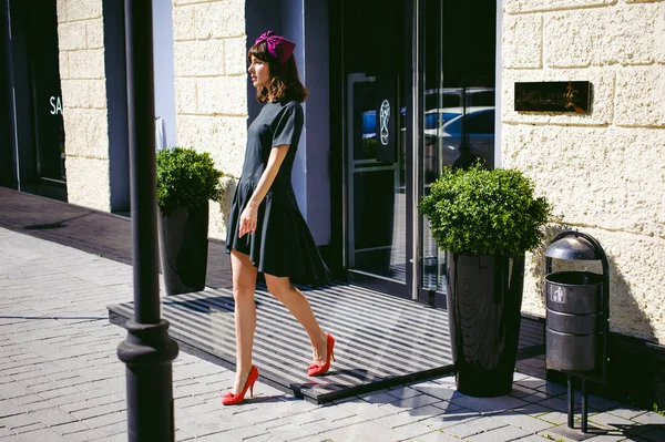 Karanlık bir şık elbiseli güzel kadın butikler yakınındaki cadde boyunca elini kolunu sallaya dönüyor. Bir moda kız portresi