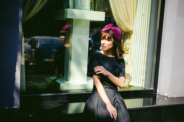 Karanlık bir şık elbiseli güzel kadın butikler yakınındaki cadde boyunca elini kolunu sallaya dönüyor. Bir moda kız portresi — Stok fotoğraf