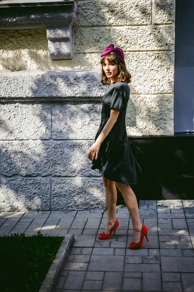 Mulher bonita em um vestido elegante escuro passeia ao longo da rua, perto de boutiques. Retrato de uma menina na moda — Fotografia de Stock