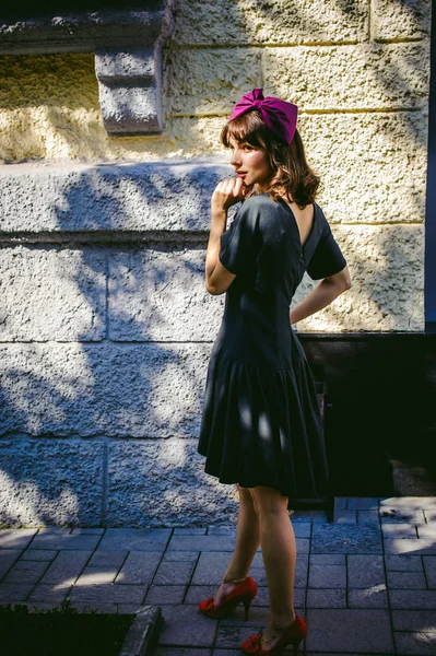 Mulher bonita em um vestido elegante escuro passeia ao longo da rua, perto de boutiques. Retrato de uma menina na moda — Fotografia de Stock