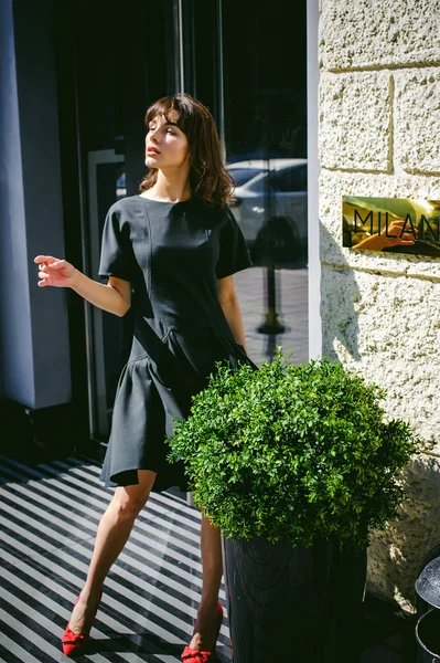 Karanlık bir şık elbiseli güzel kadın butikler yakınındaki cadde boyunca elini kolunu sallaya dönüyor. Bir moda kız portresi