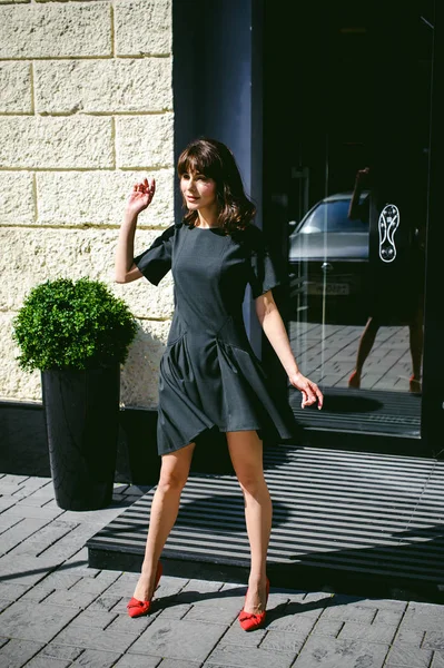 Karanlık bir şık elbiseli güzel kadın butikler yakınındaki cadde boyunca elini kolunu sallaya dönüyor. Bir moda kız portresi