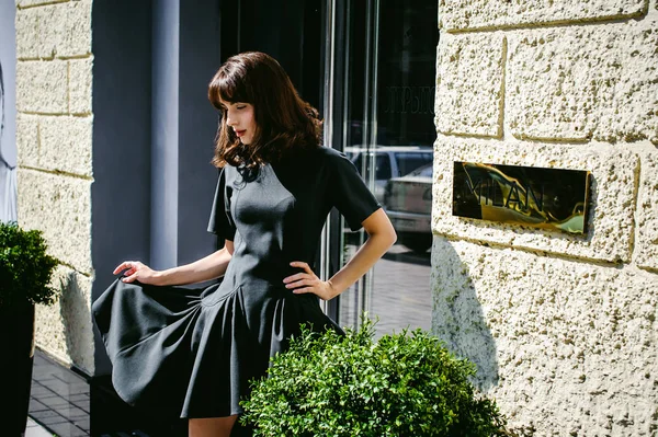 Karanlık bir şık elbiseli güzel kadın butikler yakınındaki cadde boyunca elini kolunu sallaya dönüyor. Bir moda kız portresi